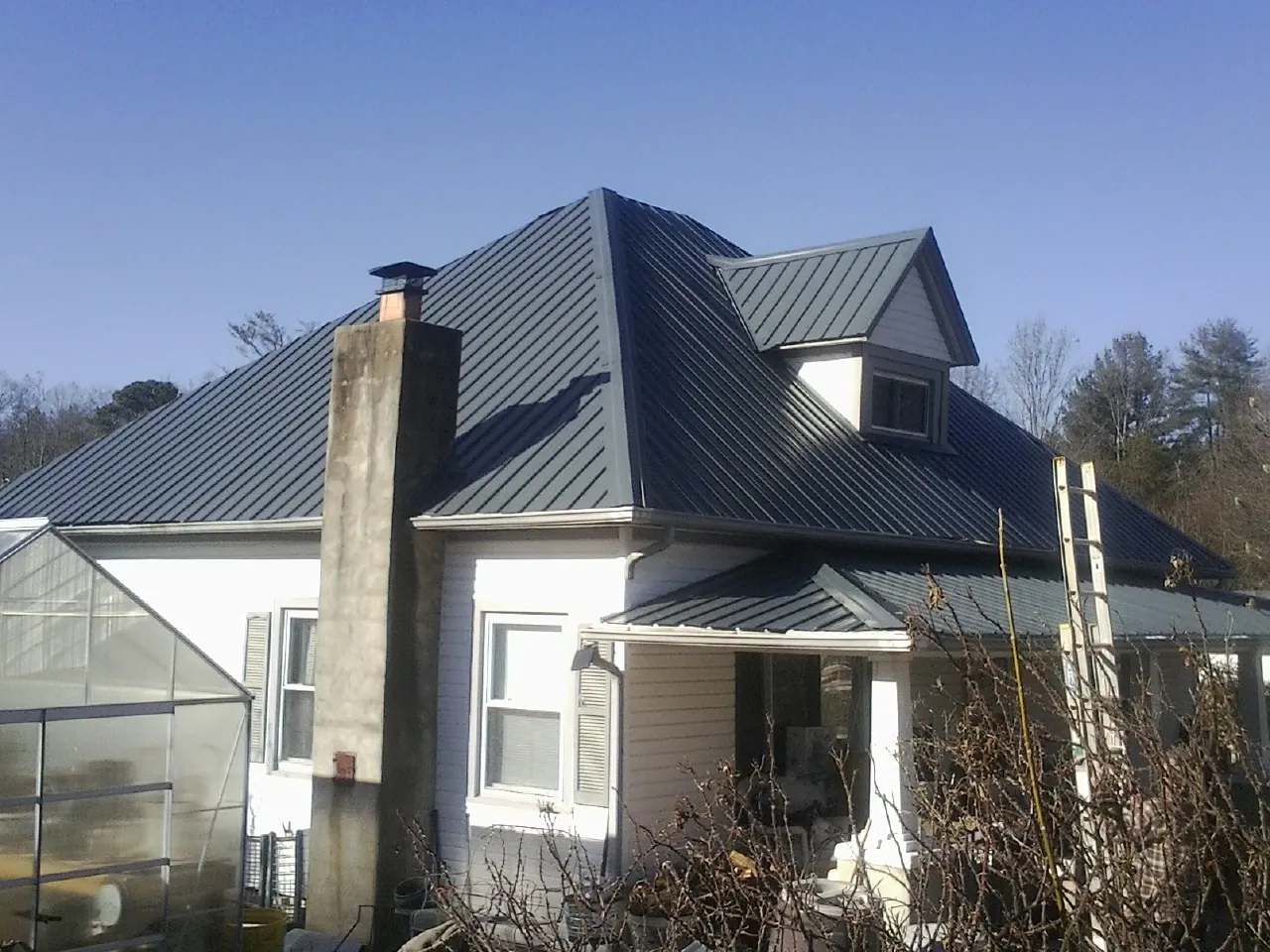 Dark blue standing seam metal roof on a white farmhouse with dormer — Slate & Tile Roof Repair by Roofing Brothers in Nunn