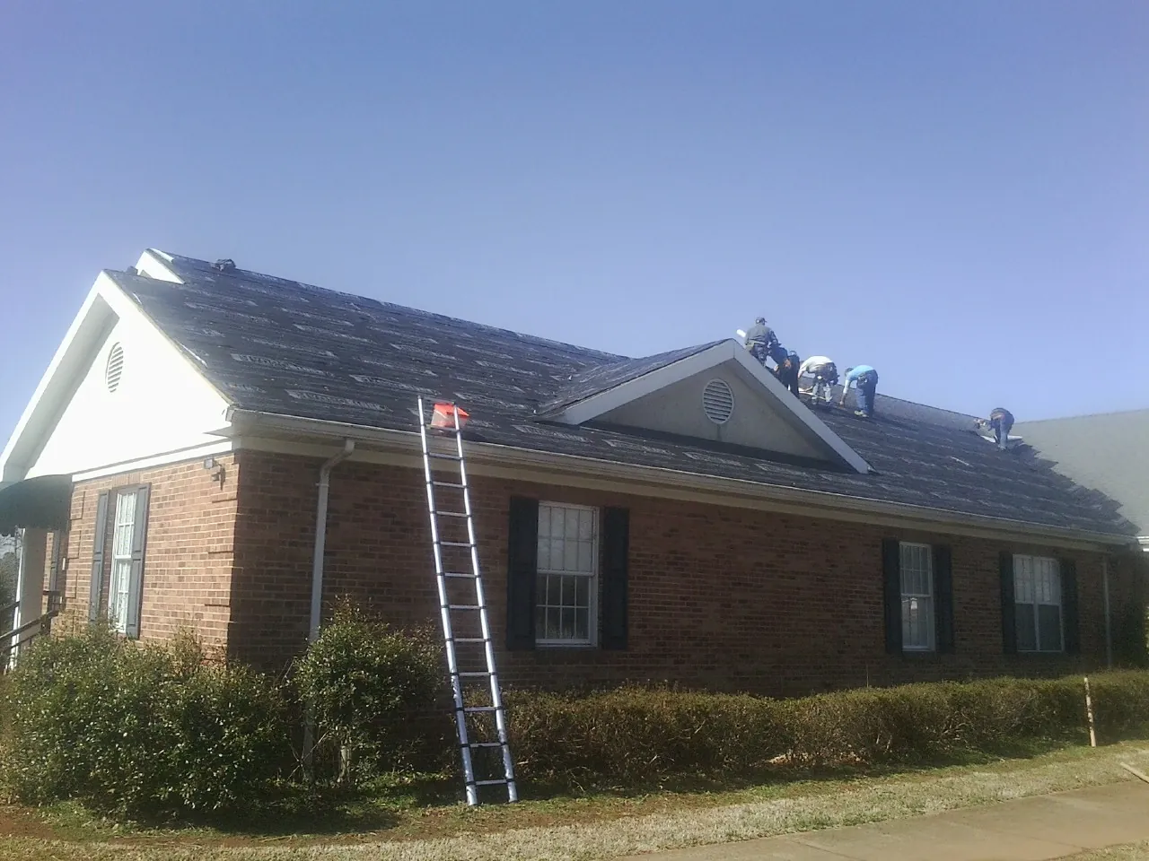 Crew tearing shingles off a brick ranch roof with a ladder set — Metal Roof Repair work by our crew in Nunn