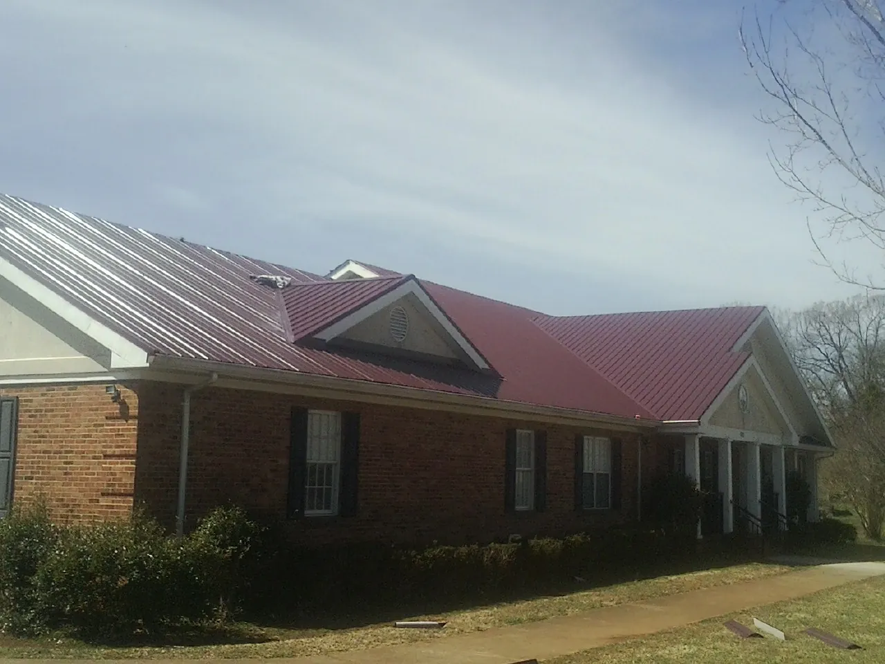 Red metal roof with gabled entries on a long brick building, from a Hail Damage Roof Repair job in Nunn