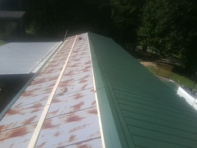 Old rusted panels beside newly installed green metal roofing — Wind Damage Roof Repair by Roofing Brothers in Nunn