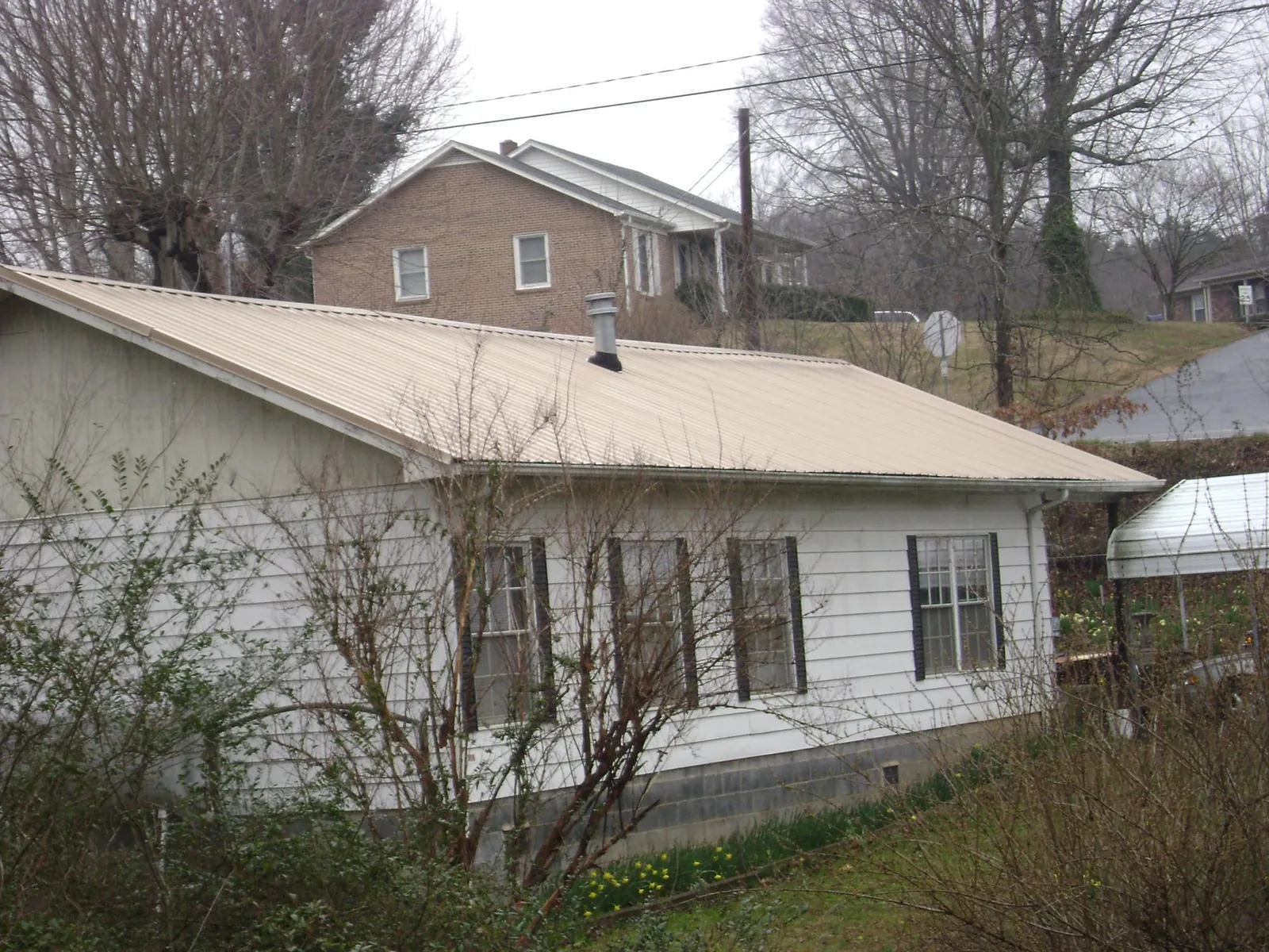 Tan metal roof on a white sided house set into a hillside — Commercial Roofing by Roofing Brothers in Nunn