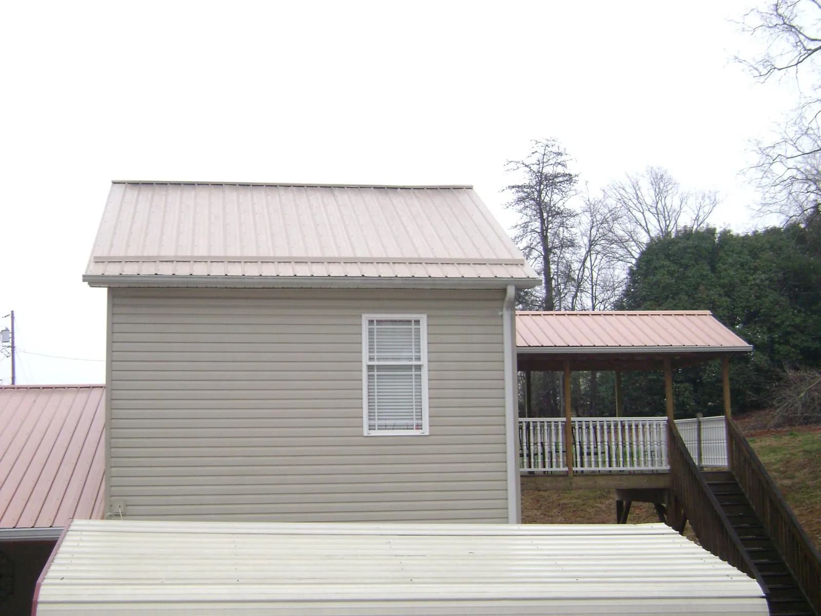 Tan metal roofs on a two story addition and attached porch, from a Roof Replacement job in Nunn